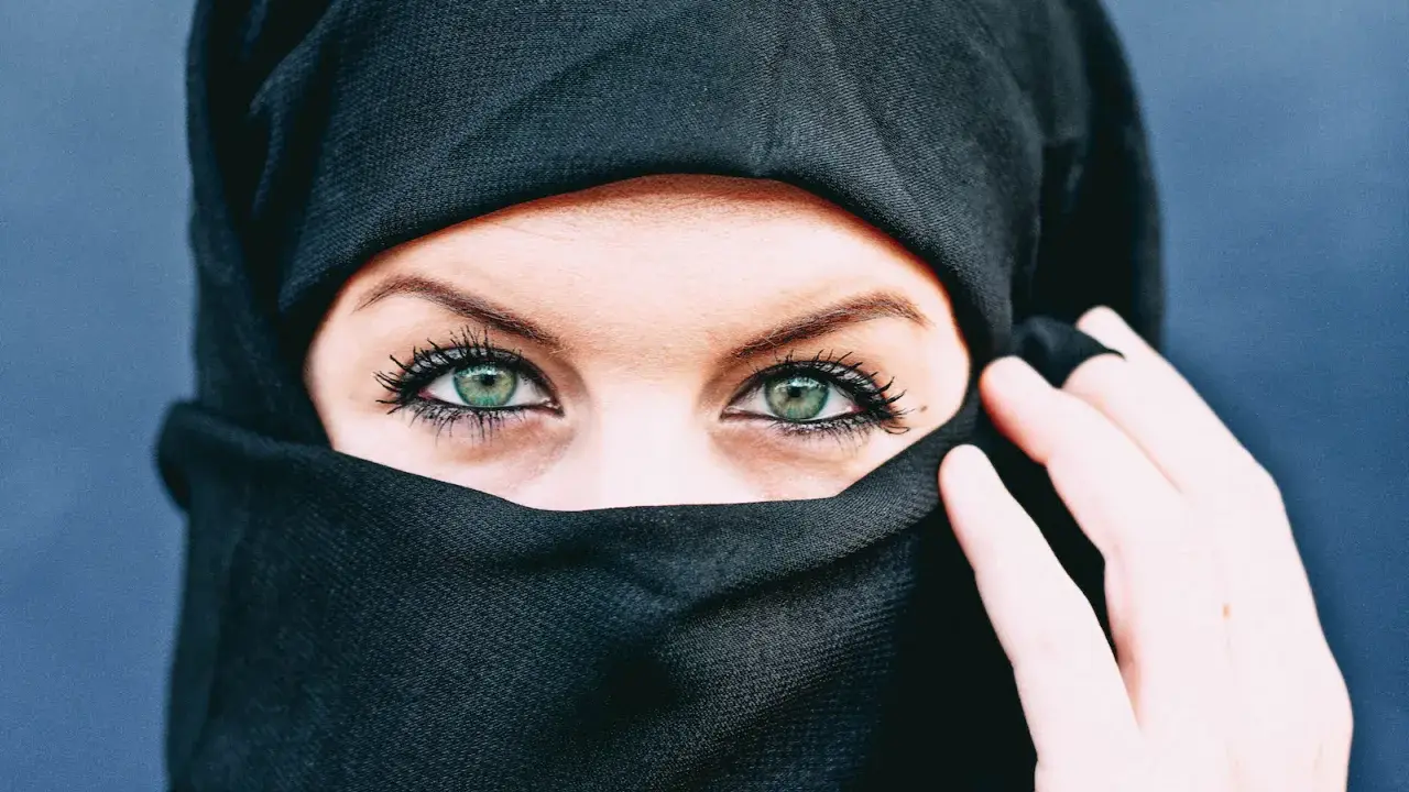 Ein schwarzes Kopftuch umrahmt ein Gesicht, dessen grüne Augen durch den Stoff blicken. Die Bedeutung von Kopftuchfarben ist vielfältig.