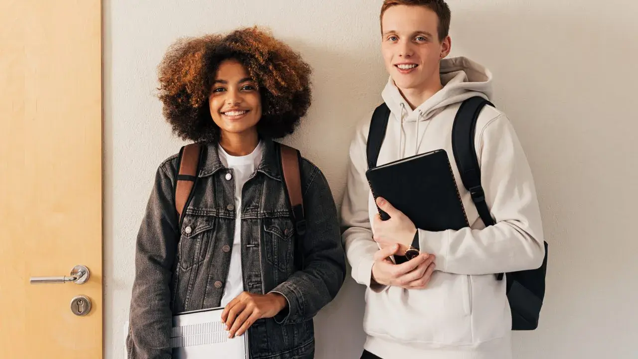 Dwóch studentów, dziewczyna z burzą włosów i chłopak z rudymi włosami, trzymają laptopy i zeszyty. To przykładowy artykuł po angielsku.