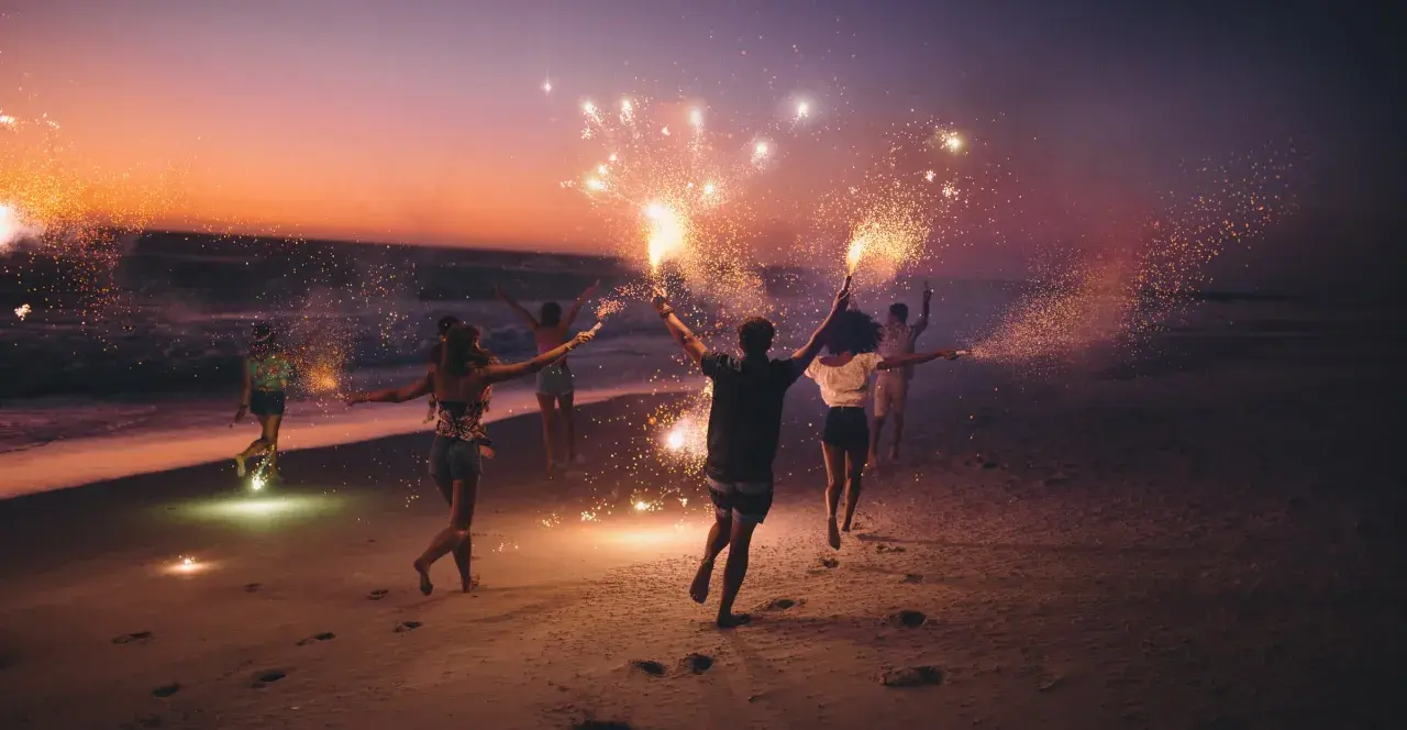 Giovani festeggiano il Ferragosto sulla Riviera Romagnola con scintille sulla spiaggia al tramonto.
