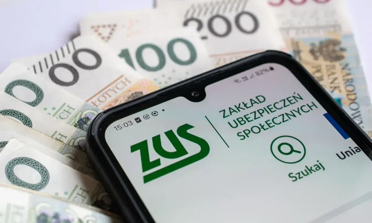 Telefon z aplikacją ZUS na tle polskich banknotów. Sprawdź, jakie odsetki ustawowe obowiązują w bieżącym roku.