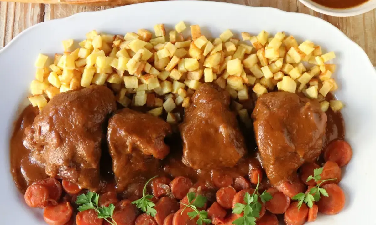 Delicioso jarrete de ternera estofado en salsa, acompañado de patatas fritas y zanahorias.