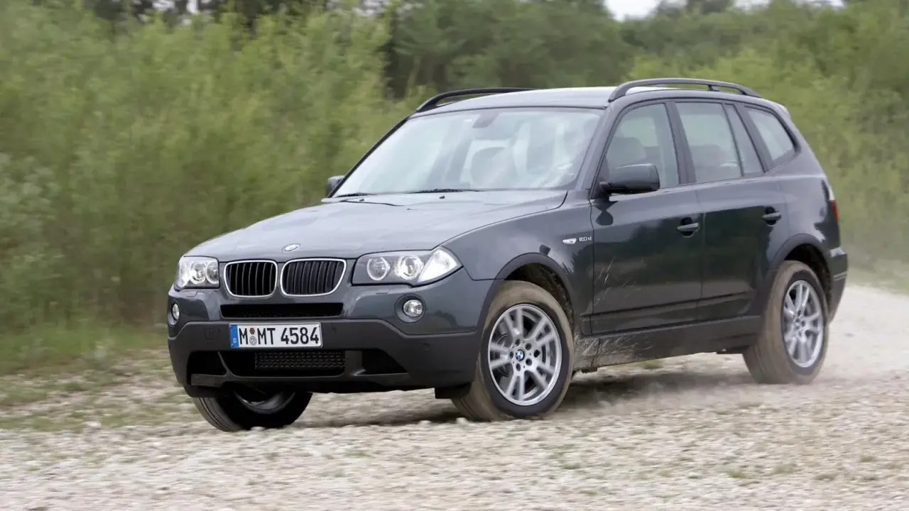 Ciemnoszary BMW X3 2024 na szutrowej drodze, otoczony zielenią.