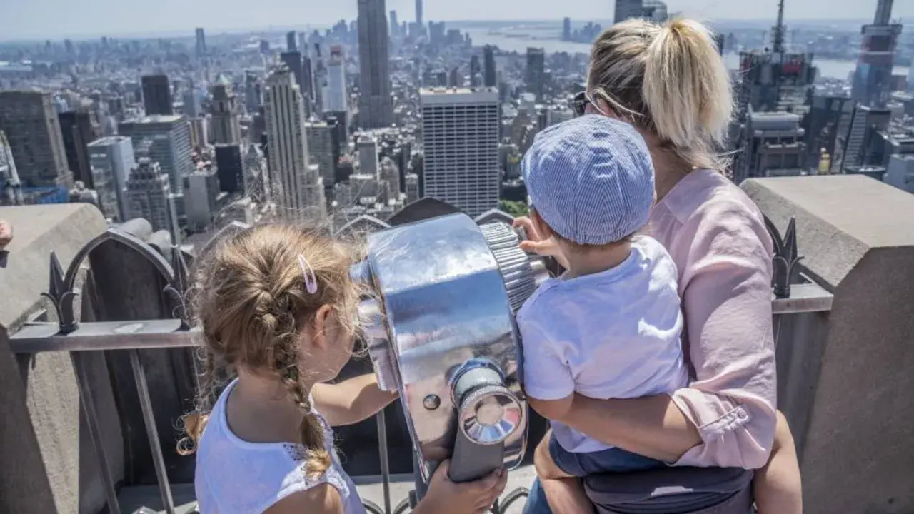 Familia disfrutando de las vistas de Nueva York con niños, explorando la ciudad a través de un telescopio.