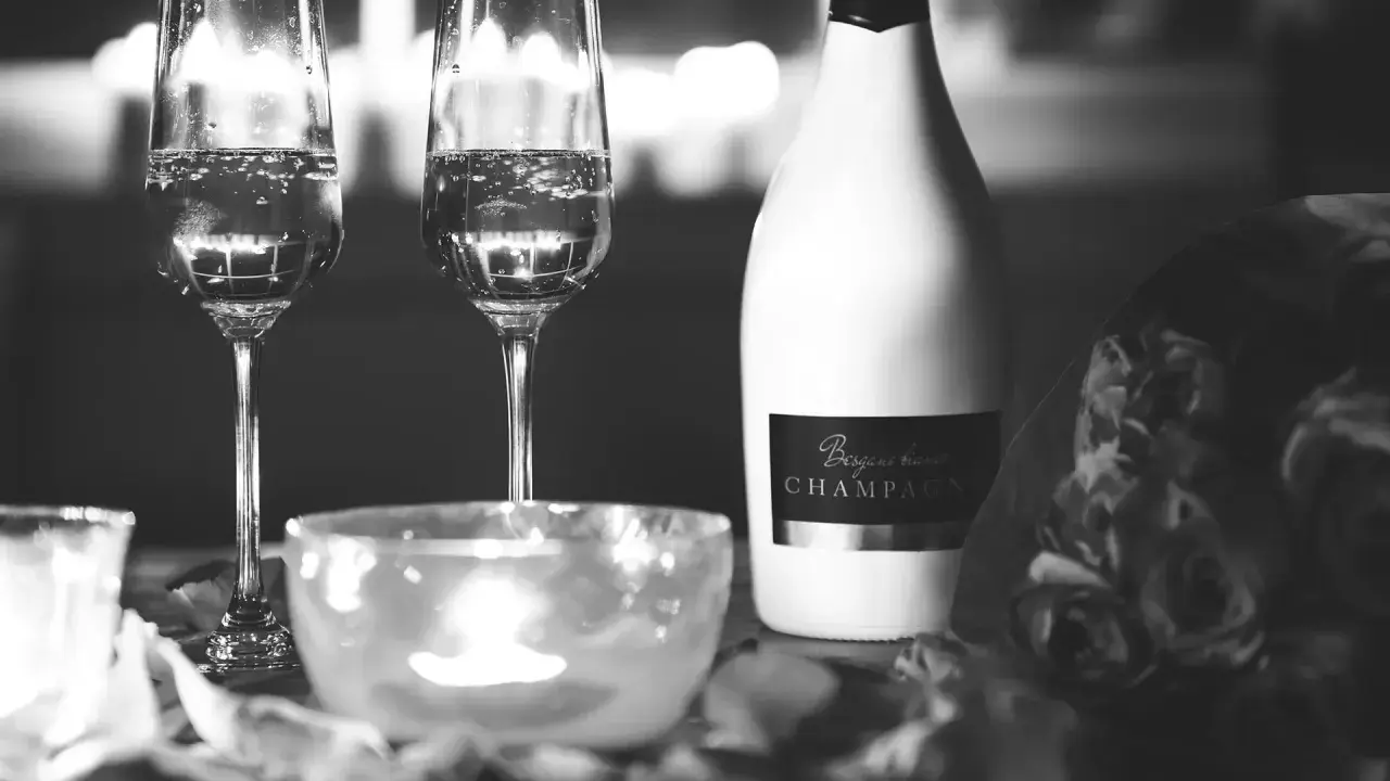 Deux flûtes de champagne pétillant, une bouteille de "Besgane bianc CHAMPAGNE" et des roses, ambiance romantique.