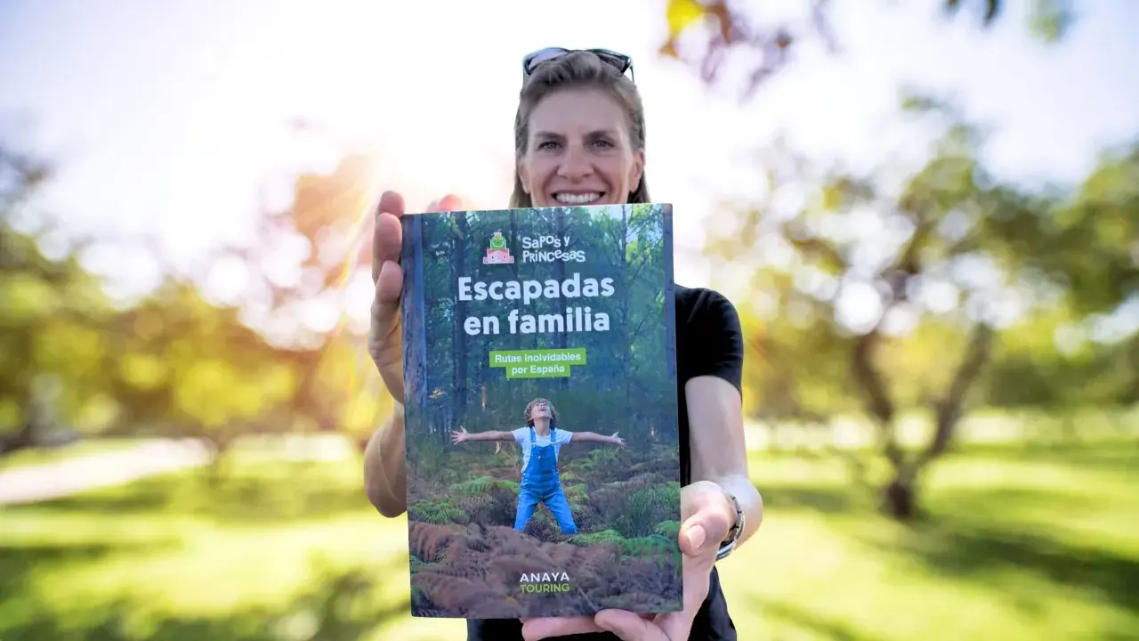 Mujer sonriente muestra libro "Escapadas en familia", con un niño en portada, ideal para viajes inolvidables para niños por España.
