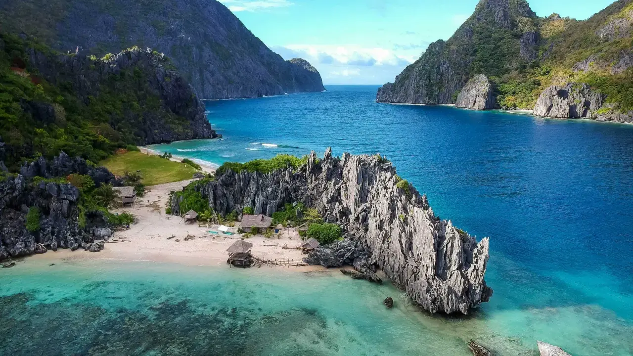 A secluded beach in the Philippines, with turquoise waters, limestone cliffs, and small huts. A perfect gay getaway in paradise.