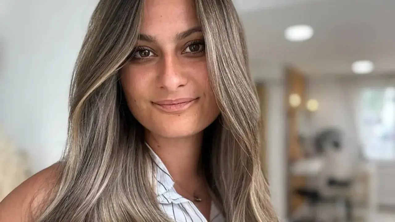 Frau mit langen, welligen Haaren in Balayage-Optik, aschblond mit helleren Strähnen. Ihr Blick ist warm und einladend.