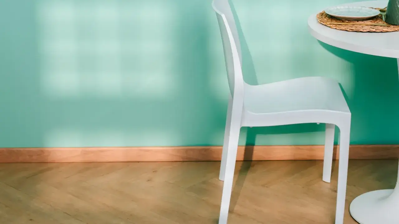 Un battiscopa in legno chiaro completa l'arredamento di una stanza con parete verde acqua, sedia bianca e tavolo.