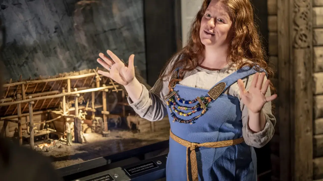 En guide i vikingakläder berättar vid en modell av en vikingaby på ett wikinger museum i Stockholm.