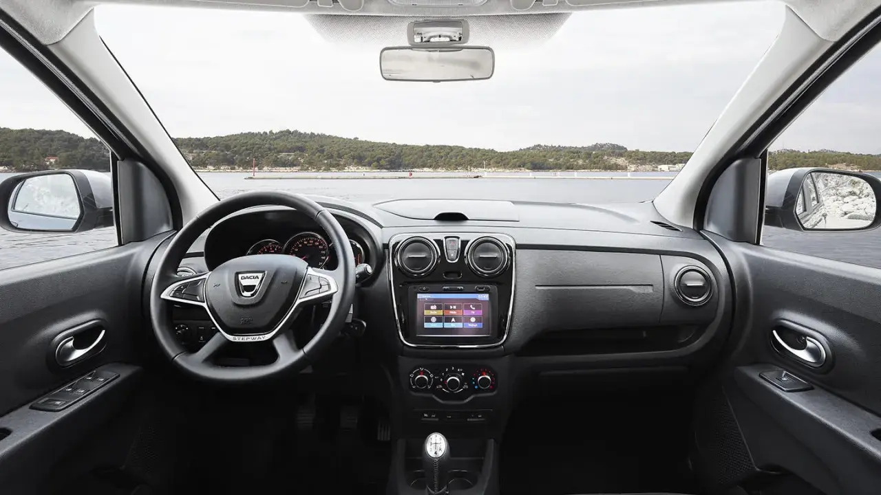 Interior del Dacia Lodgy con volante, pantalla táctil y palanca de cambios. El paisaje marino se ve a través del parabrisas.