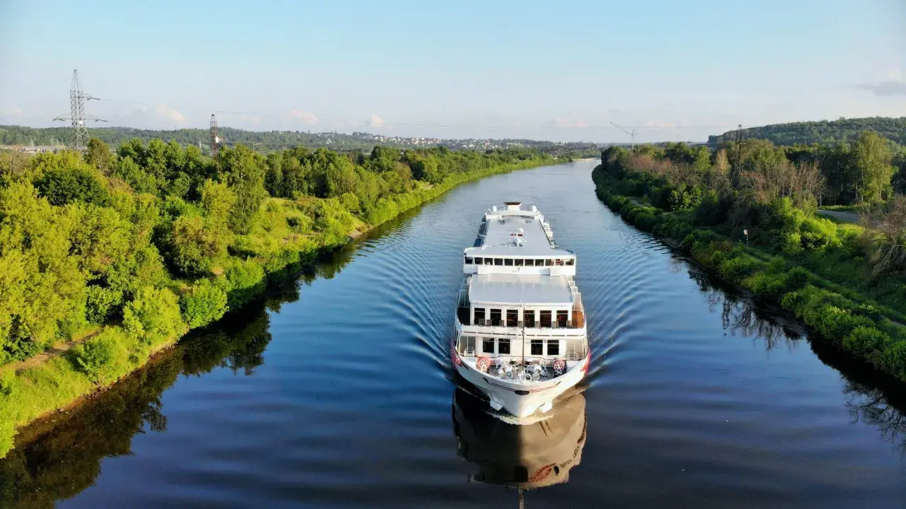 Nave da crociera solca un fiume sereno, con rive alberate che ricordano la bellezza naturale vicina alla capitale Russia.