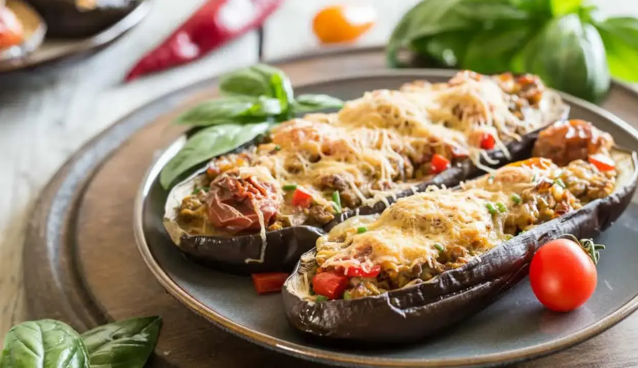 Berenjenas rellenas de atún, gratinadas con queso y decoradas con albahaca y tomate. Un plato delicioso y fácil de preparar.