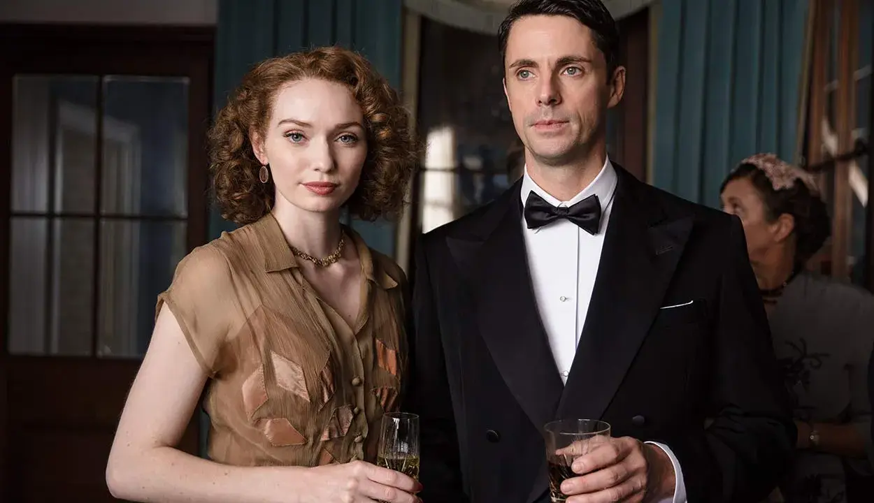 Ett elegant par med drinkar i handen, en scen från huset på udden serie. Kvinnan bär en brun klänning, mannen en smoking.
