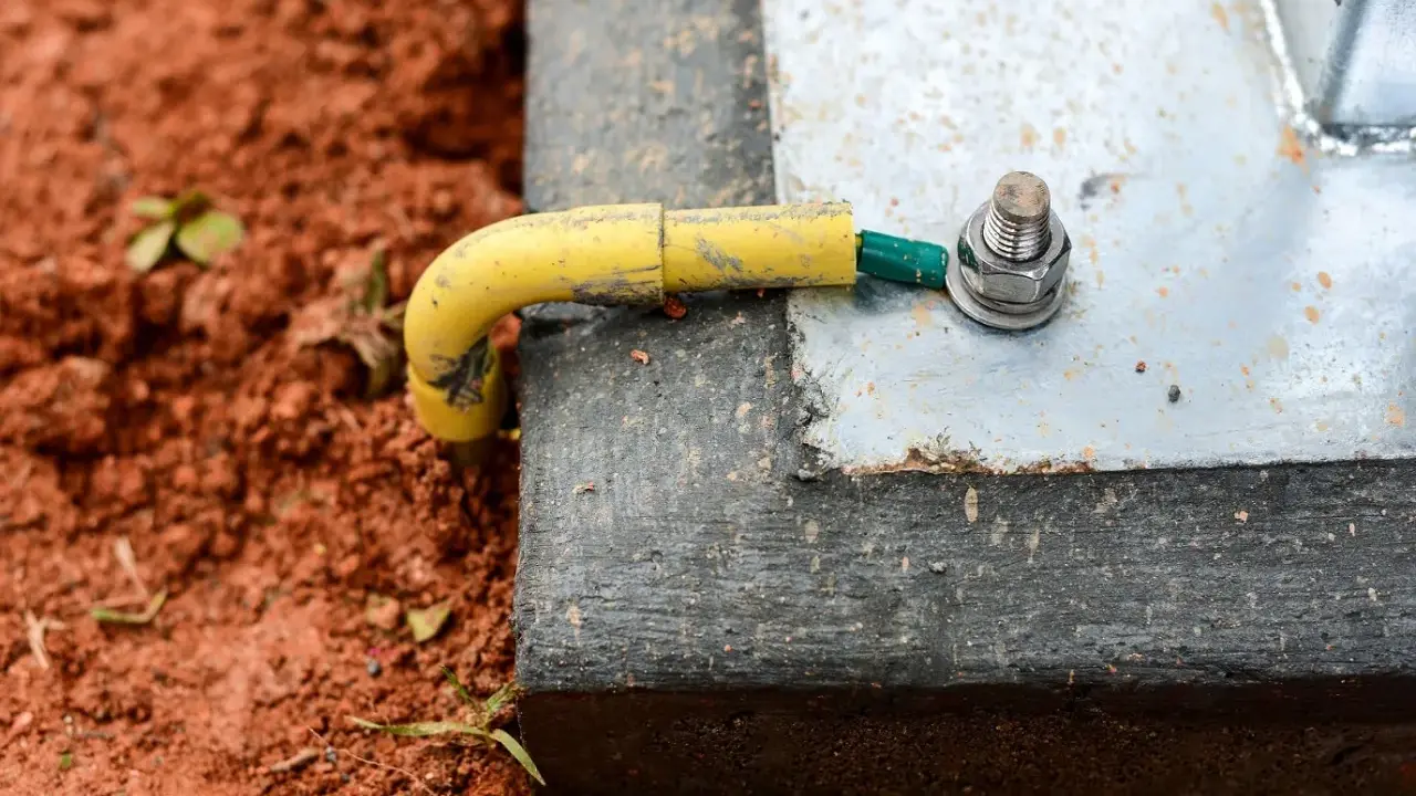 Connexion de la prise de terre maison à une structure métallique, assurant la sécurité électrique. Le câble jaune est relié à une cosse verte, fixée par un boulon.