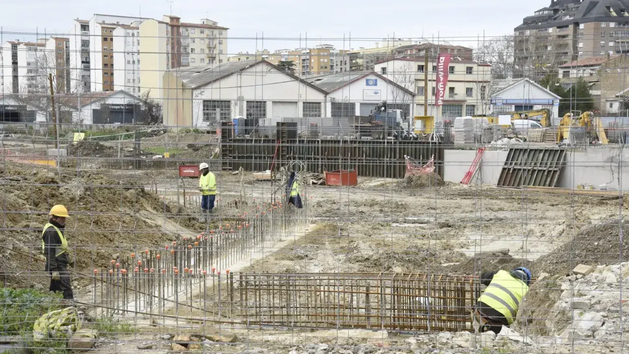 Obreros trabajan en la preparación de cimientos para nuevos proyectos de construcción. Se ven varillas de acero y maquinaria pesada en un día nublado.