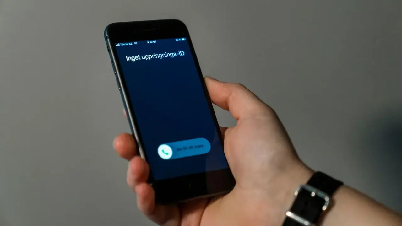 En hand håller en mobiltelefon med ett inkommande samtal. Skärmen visar "Inget uppringnings-ID" och en knapp för att svara.