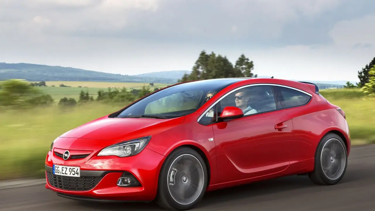 Czerwony Opel Astra J 1.4 Turbo z parą na pokładzie przemierza malowniczą trasę wśród zielonych pól i wzgórz.