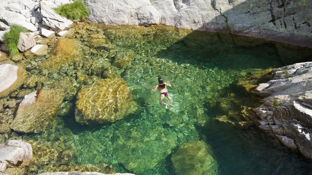 Una persona nada en unas cristalinas piscinas naturales Gredos, rodeadas de rocas y vegetación.