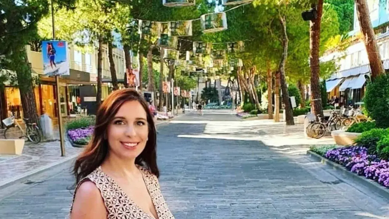 Donna sorridente in una strada alberata con negozi e fiori viola, un'atmosfera estiva nel centro di Milano Marittima.