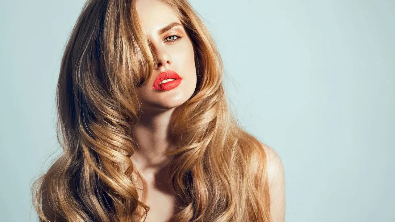 Kobieta z burzą falujących, blond włosów w stylu wolf cut, z wyrazistą czerwoną szminką.