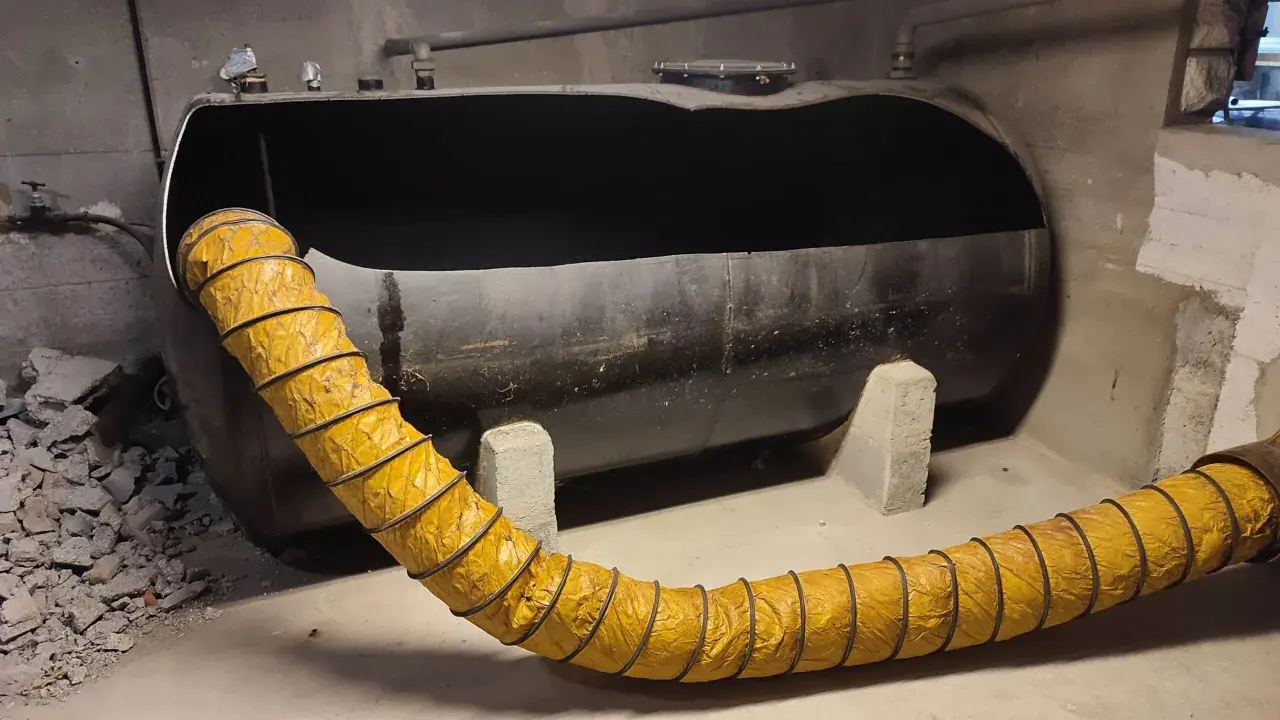 Gros réservoir de fioul noir, vide, avec un tuyau jaune flexible. Projet ma prime rénov cuve fioul en cours.