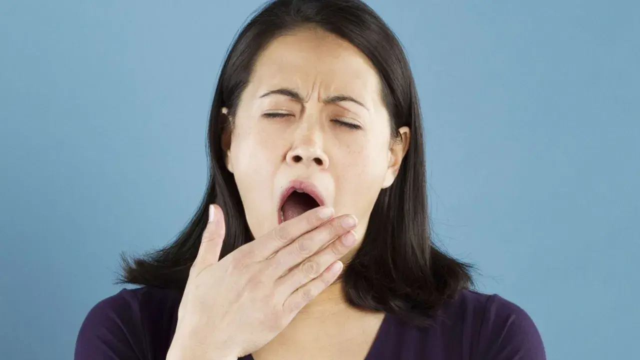 Une femme bâille, la main devant la bouche. Elle semble avoir besoin d'une pause pour réviser la conjugaison.