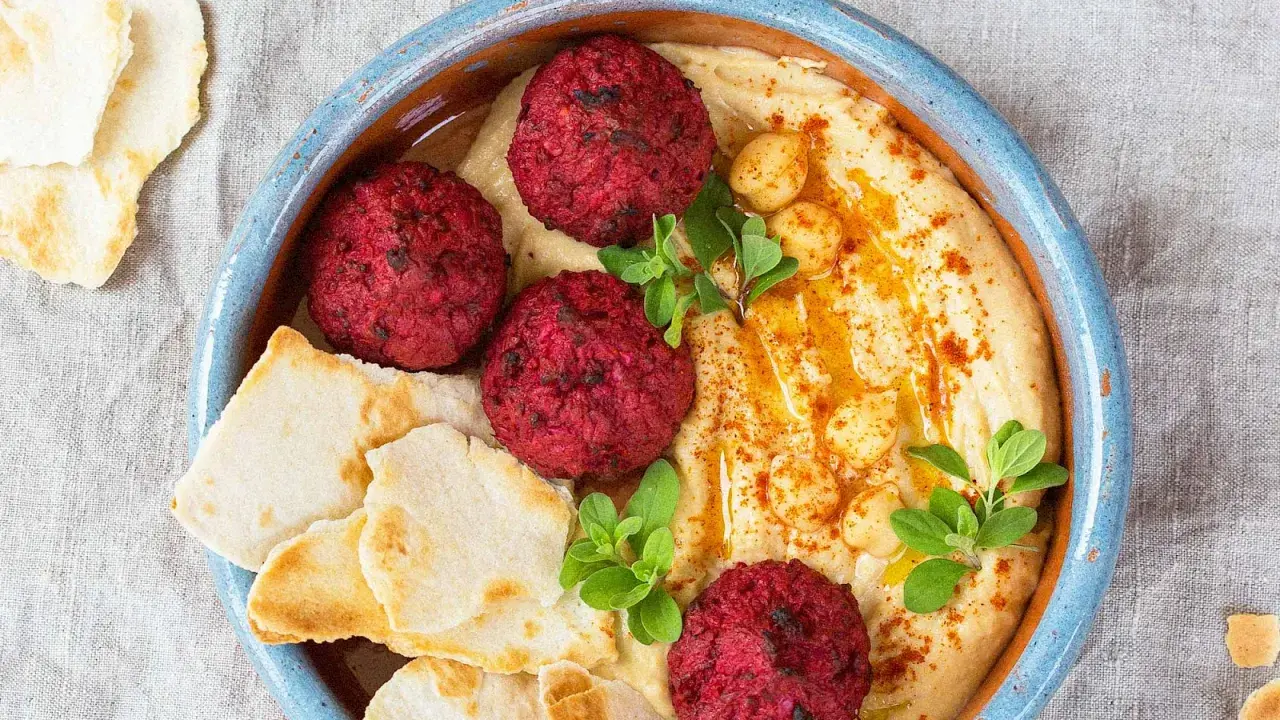 Rote Bete Falafel auf cremigem Hummus, garniert mit Kichererbsen und frischen Kräutern, serviert mit Pitabrot.