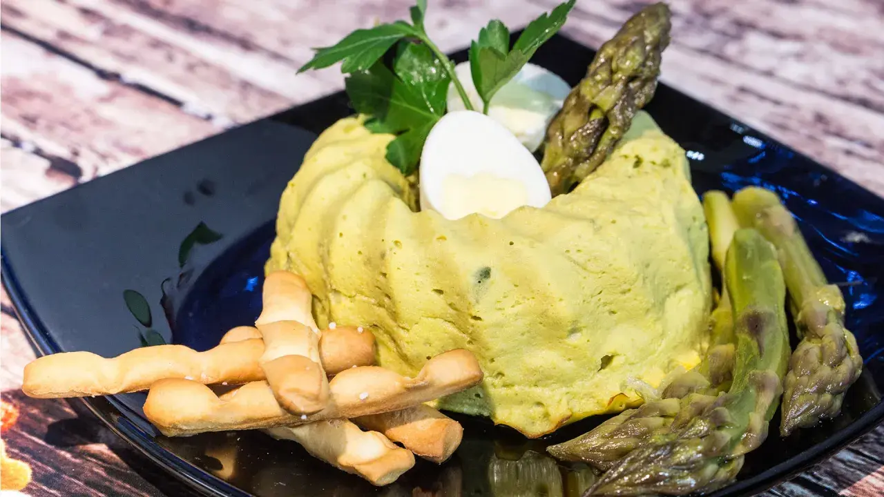 Delizioso flan di asparagi, guarnito con uovo sodo, asparagi freschi e grissini croccanti su un piatto nero.