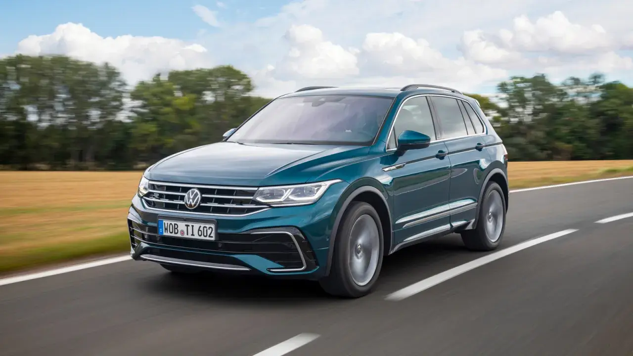 Un Volkswagen Tiguan R-Line verde oscuro se desplaza por una carretera rural, con campos dorados y árboles borrosos al fondo.