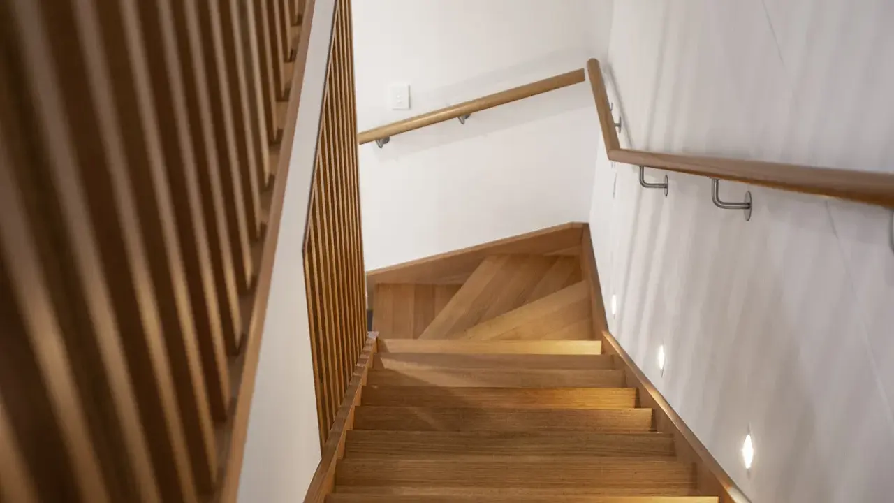 Drewniane stopnie i nowoczesna lamperia na klatce schodowej tworzą ciepłą, przytulną atmosferę.