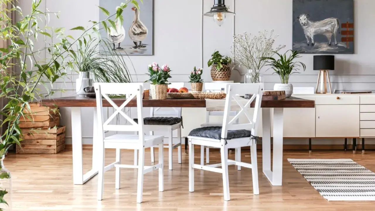 Comedor con mesa de madera oscura y sillas blancas, un ejemplo perfecto de cómo combinar muebles blancos y madera oscura. Plantas y cuadros decoran el espacio.