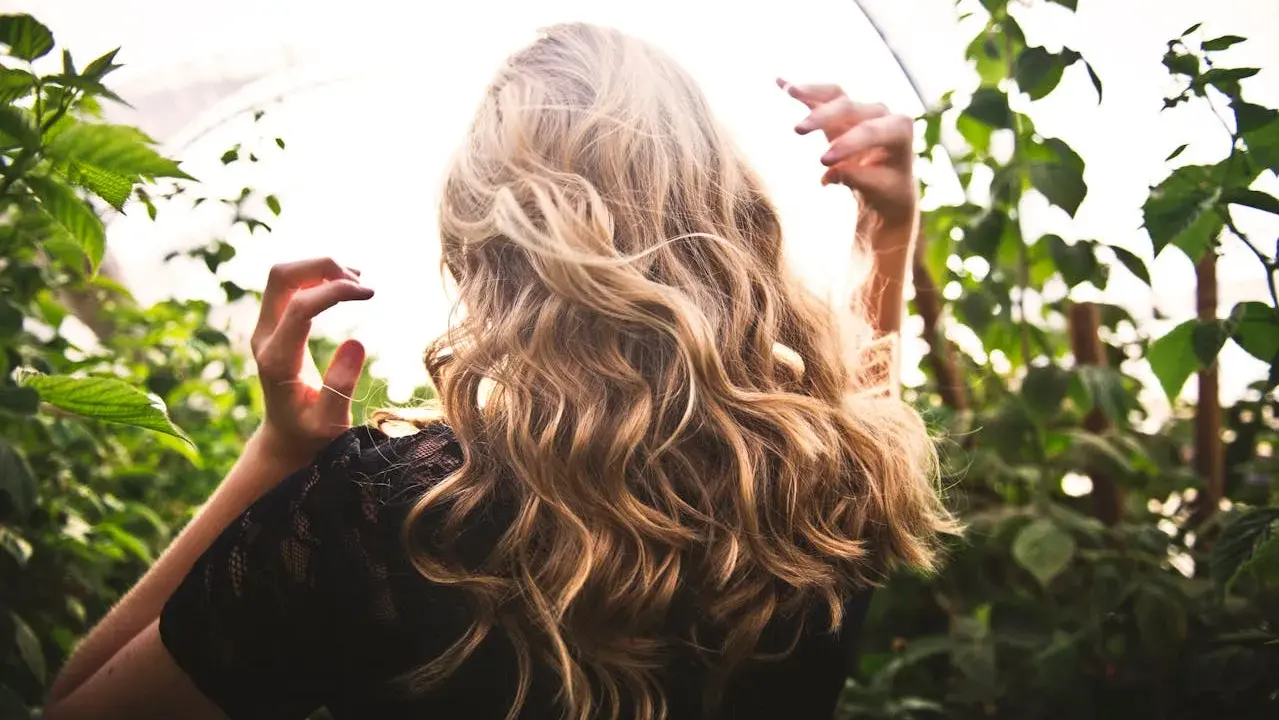 Capelli biondi mossi con sfumature naturali, che ricordano la differenza tra meches e balayage, tra il verde delle piante.