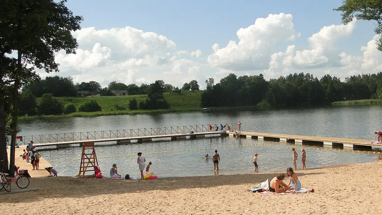 Słoneczny dzień na jednej z najpiękniejszych plaż na Mazurach. Ludzie odpoczywają na piaszczystym brzegu i w wodzie, ciesząc się latem.