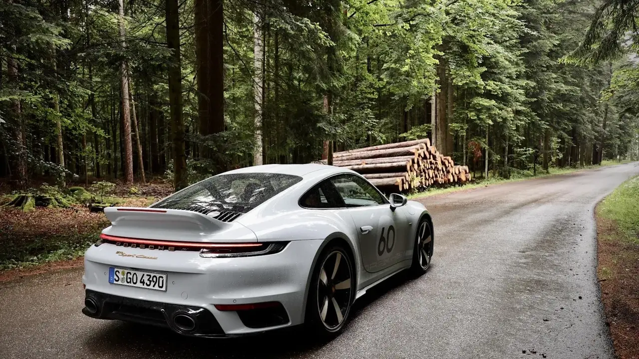 Ein weißer Porsche 911 mit der Nummer 60 auf der Seite fährt auf einer nassen Waldstraße. Die Beschleunigung von 0 auf 100 km/h ist beeindruckend.