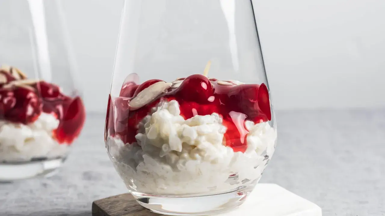 Delicioso arroz con leche asturiano cremoso, coronado con cerezas rojas y almendras laminadas en un vaso.