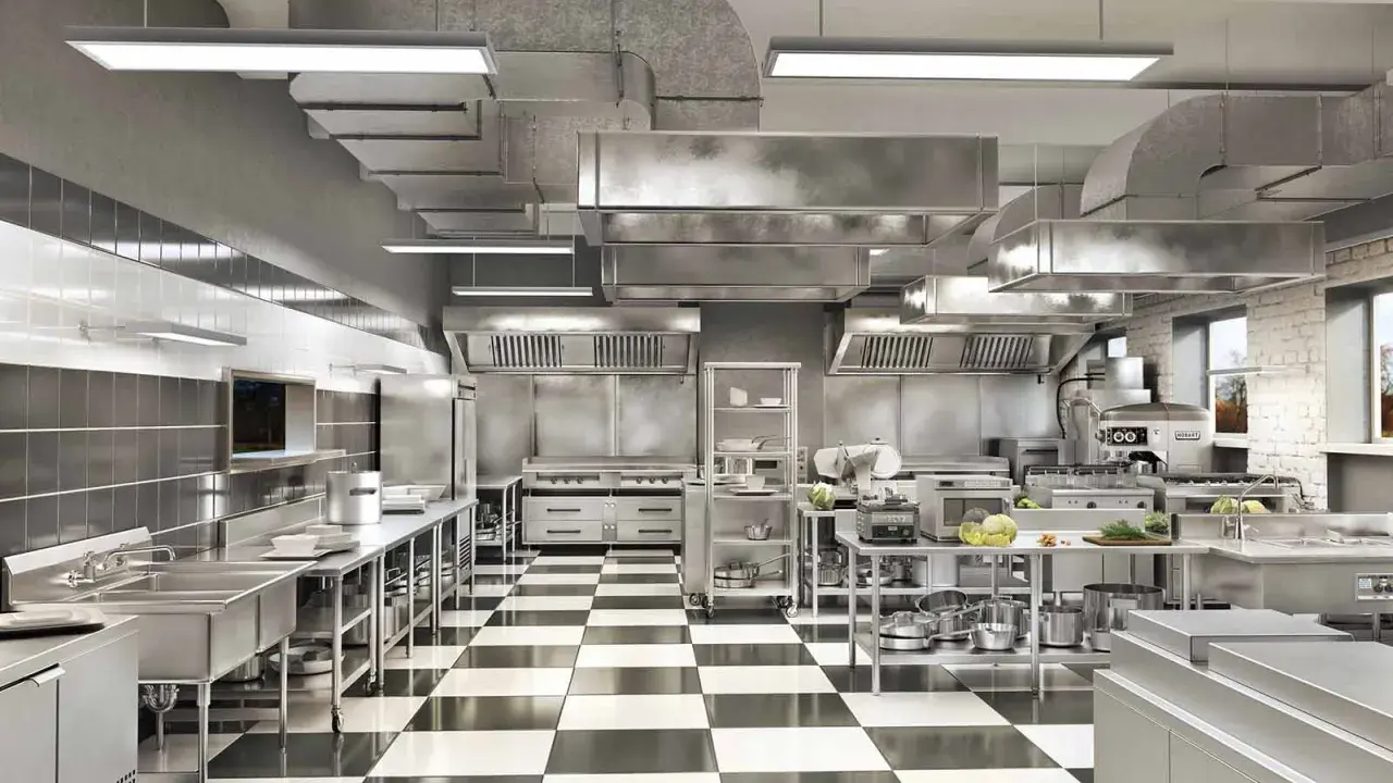 Cocina profesional de acero inoxidable con suelo de baldosas a cuadros, campanas extractoras y equipamiento listo para cualquier tipo de cocina.