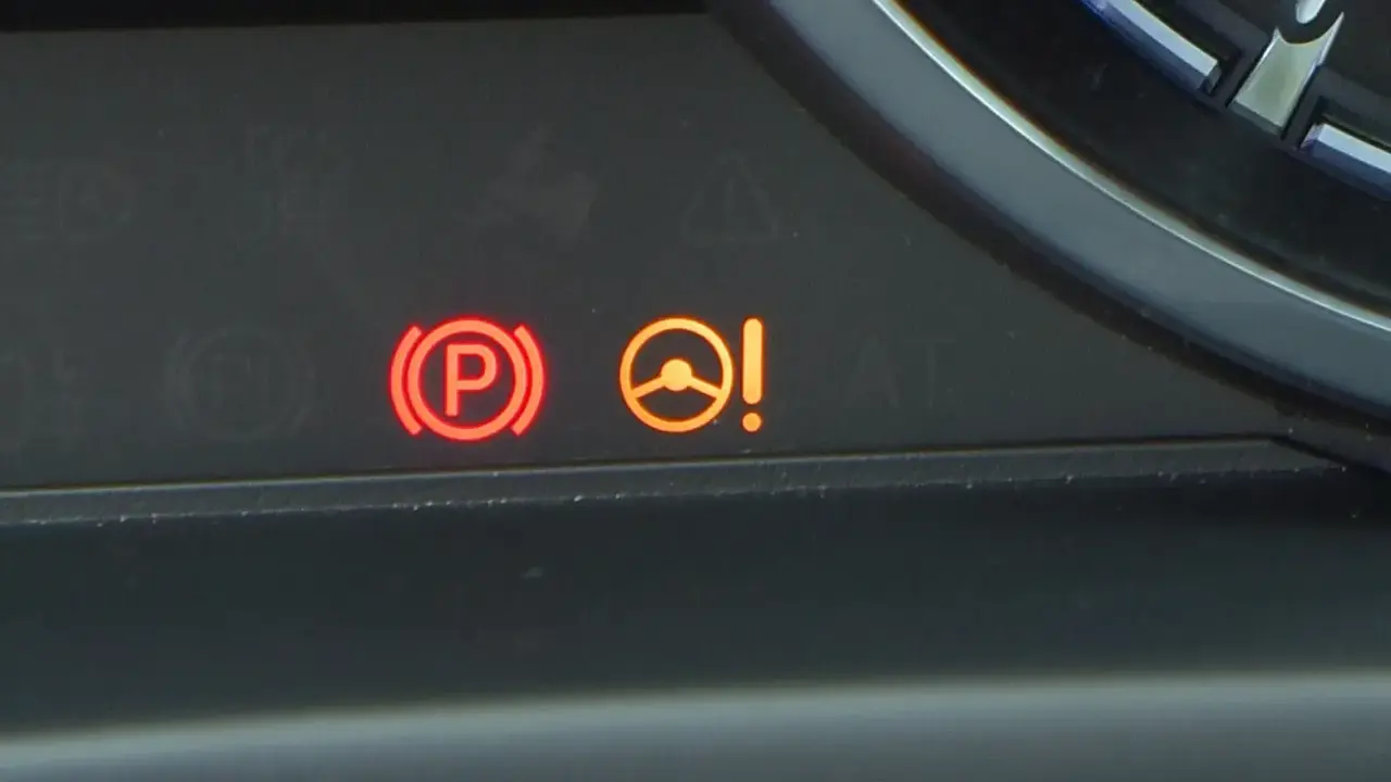 Kontrolka PS Nissan: czerwony symbol hamulca ręcznego i pomarańczowa kontrolka układu kierowniczego z wykrzyknikiem.