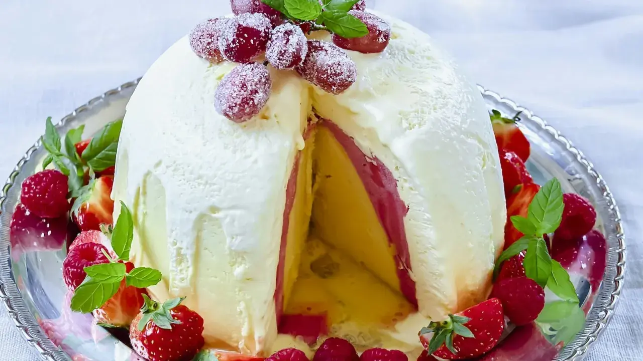 En imponerande dessert till nyår: en kupolformad glassbakelse med lager av gul och rosa glass, dekorerad med färska bär och mynta.