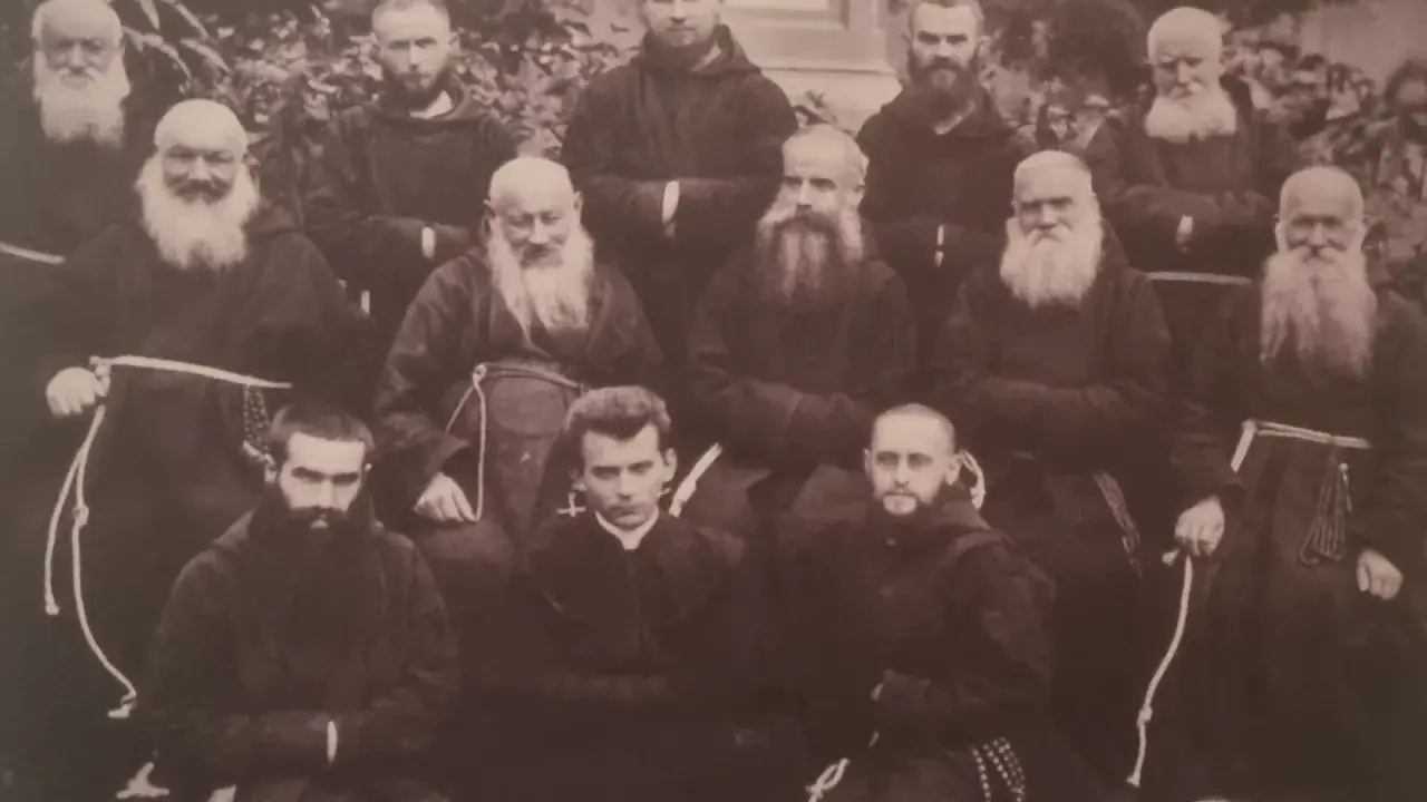 Grupa zakonników w habitach. W środku, w pierwszym rzędzie, siedzi młody mężczyzna, być może to **Honorat Koźmiński** w otoczeniu braci.
