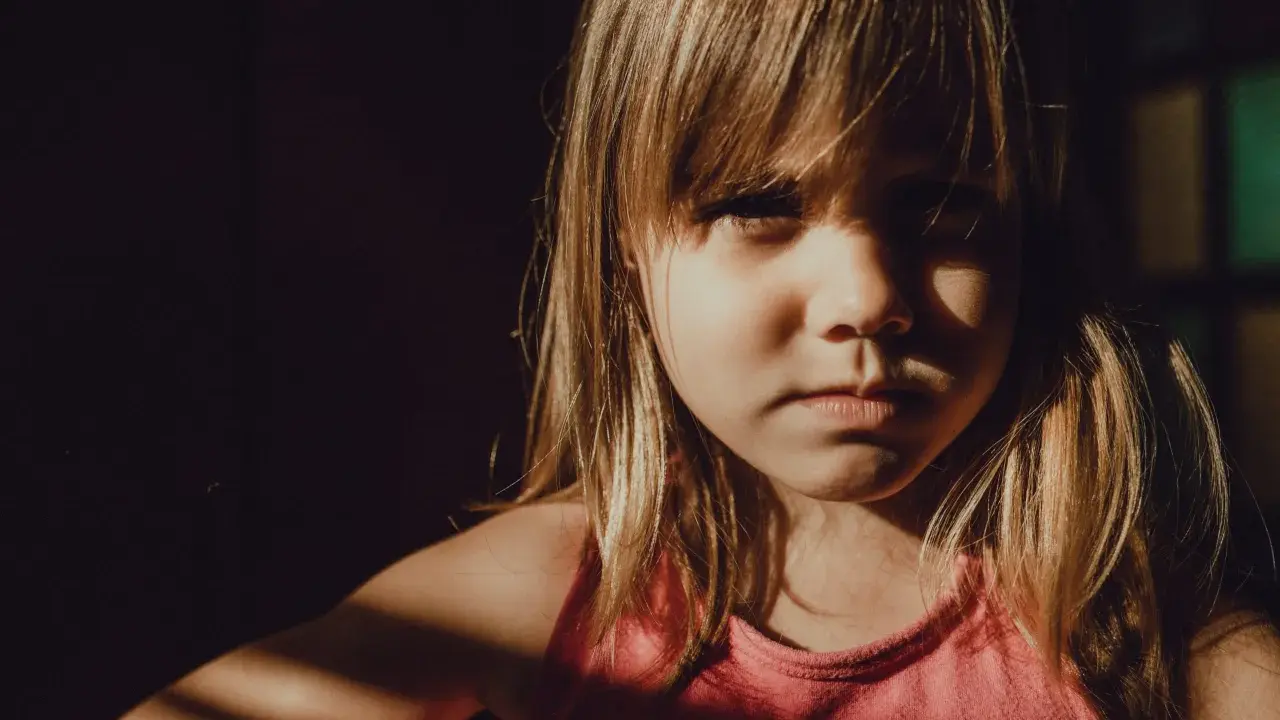 Niña con expresión seria, con luz de ventana en su rostro. A veces, mi hijo de 9 años se enoja por todo, pero hoy solo mira con intensidad.