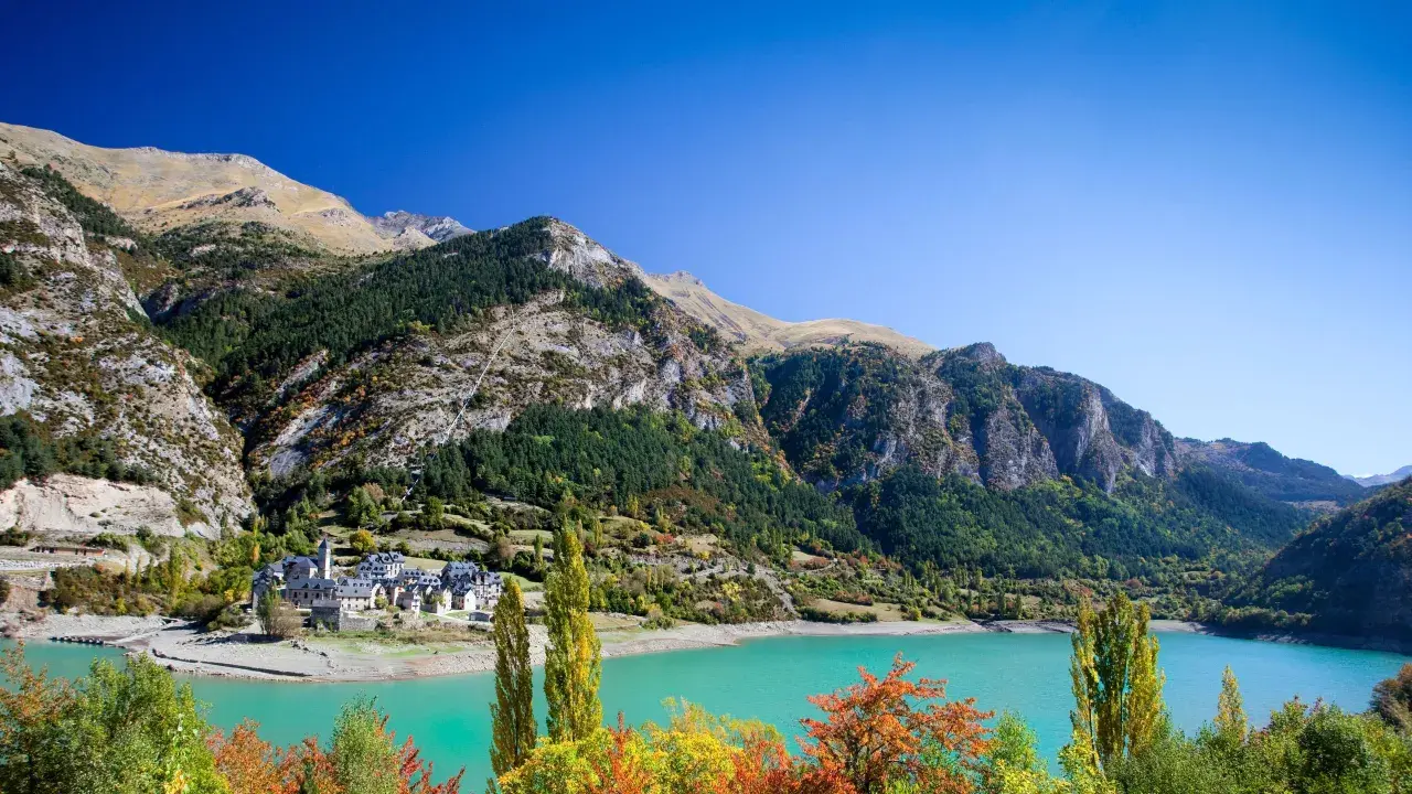 Pueblo de Lanuza, Huesca, con su embalse de aguas turquesas y montañas verdes.