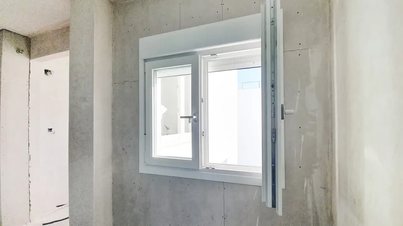 Instalar ventana PVC en obra gris. Ventana blanca de doble cristal con manilla plateada, lista para ser fijada.