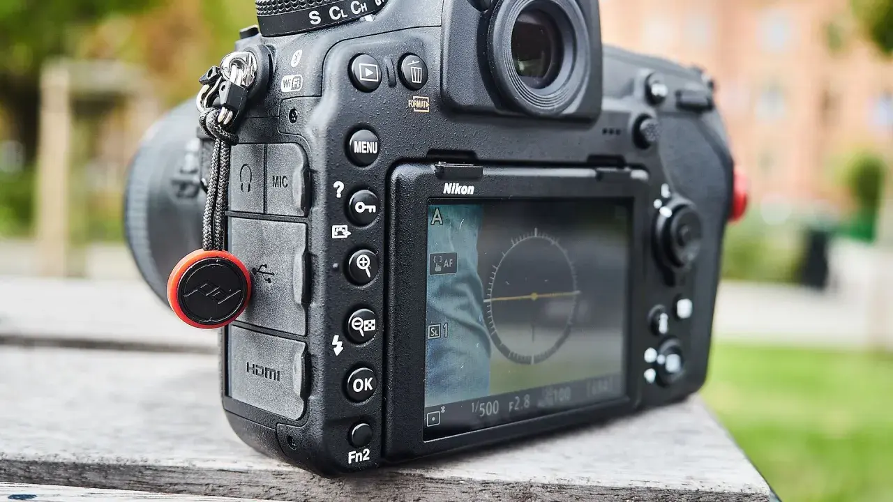 Nikon D850 test w plenerze. Aparat leży na drewnianym stole, w tle zieleń i budynek.