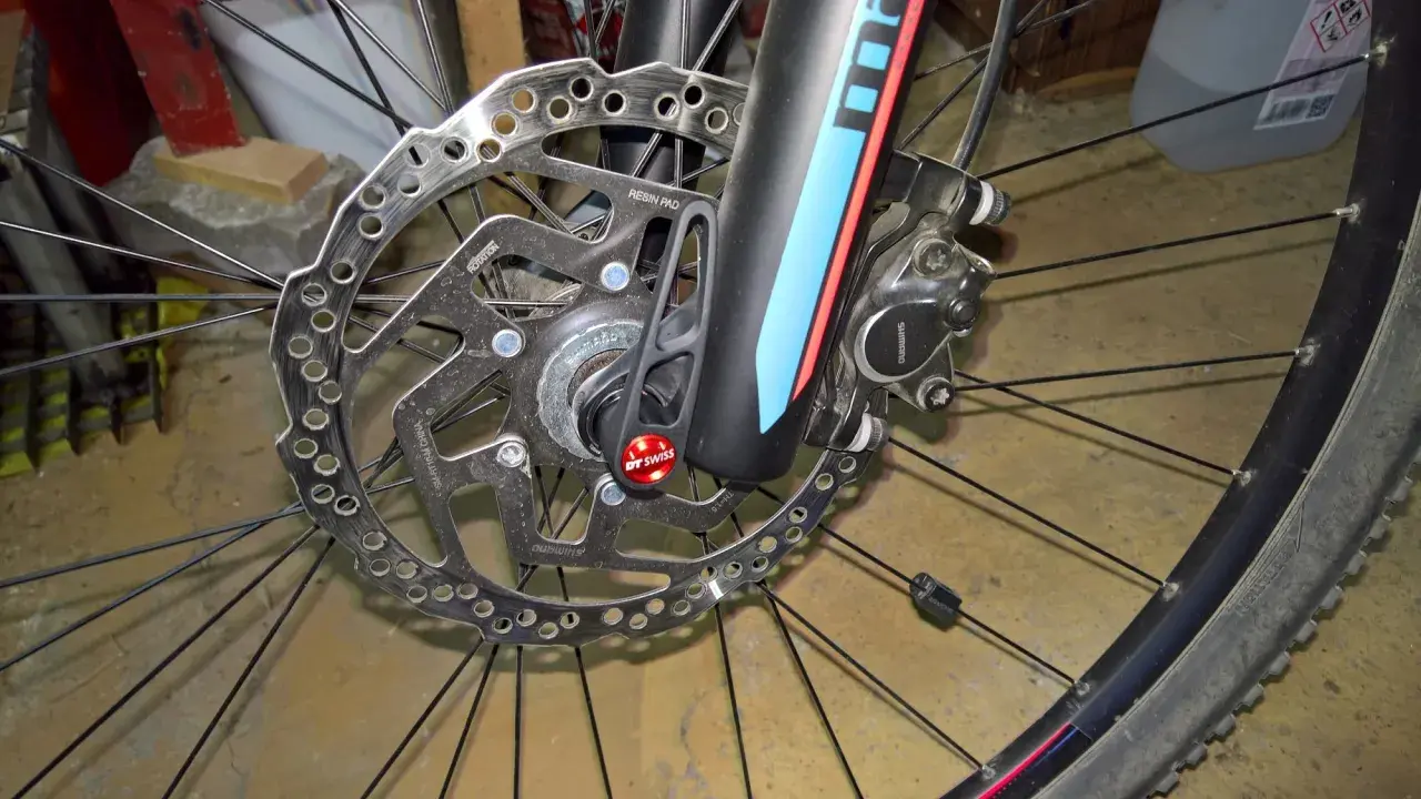 Hamulec tarczowy roweru z mocowaniem **center lock**. Widoczna tarcza hamulcowa Shimano, zacisk i szybkozamykacz DT Swiss.