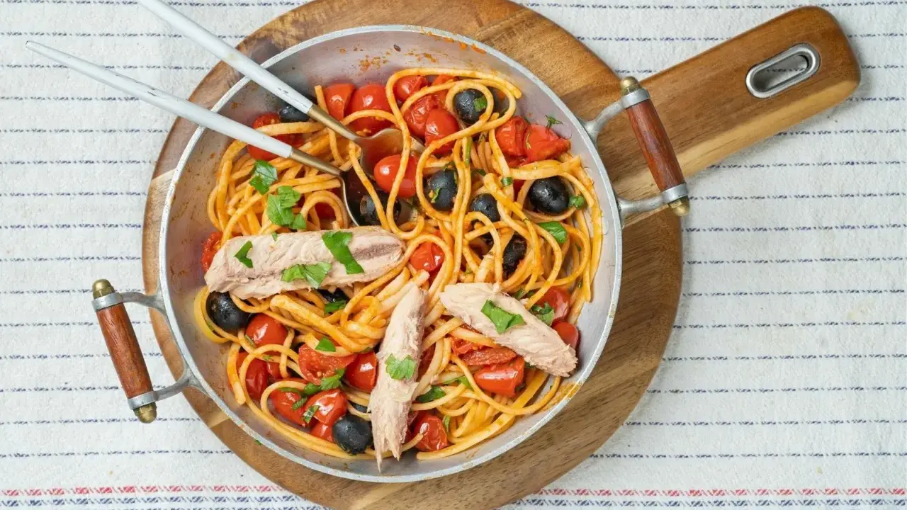 Pyszne spaghetti alla puttanesca z tuńczykiem, pomidorkami i czarnymi oliwkami w metalowej patelni, gotowe do podania.