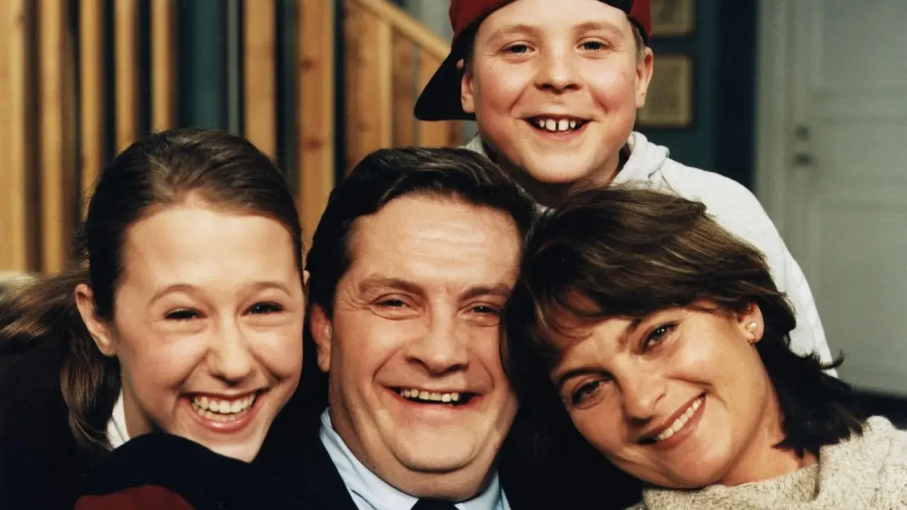 En glad familj, som hämtad ur svenska komedier, ler mot kameran. Pappa, mamma, dotter och son.