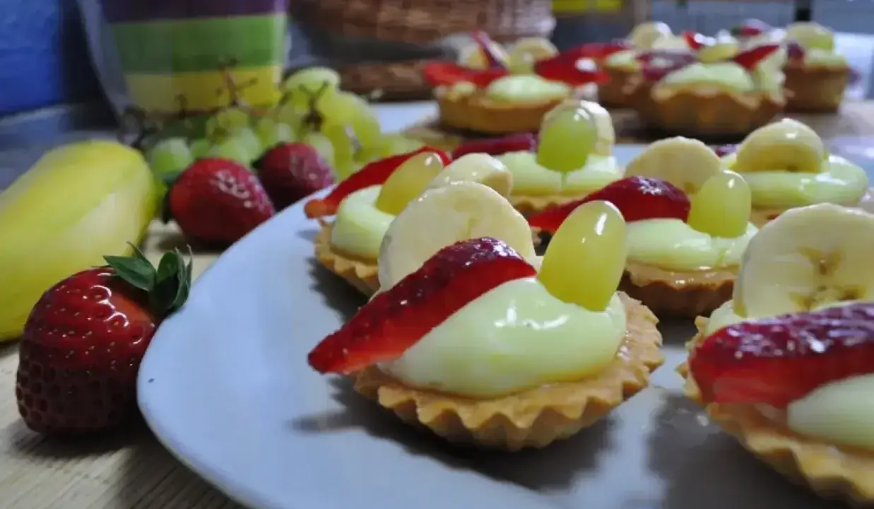 Pyszne babeczki z budyniem, udekorowane truskawkami, bananami i winogronami, wyglądają apetycznie.