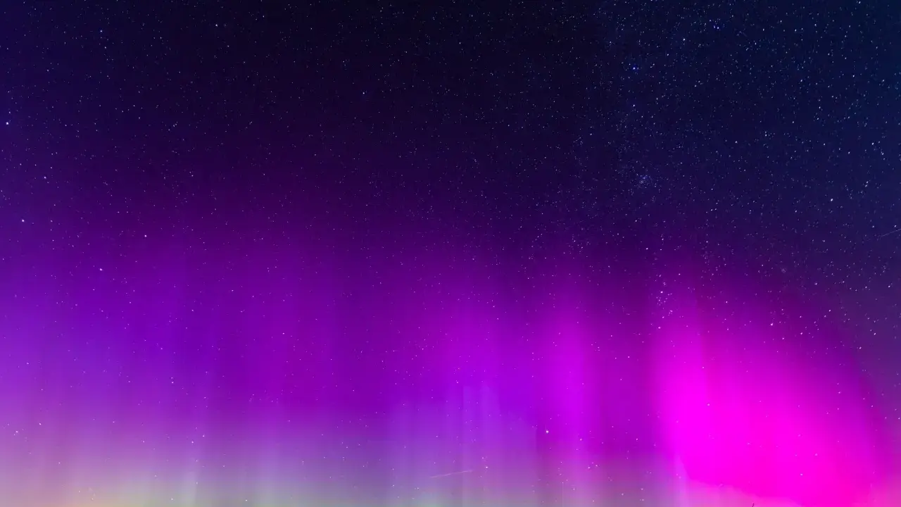 Nocne niebo rozświetlone fioletową i zieloną zorzą polarną, kiedy jest zorza polarna. Gwiazdy migoczą nad ciemnym horyzontem.