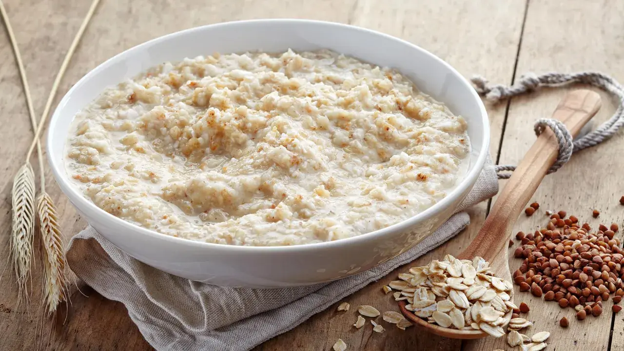 Schüssel mit Haferbrei, daneben Haferflocken und Buchweizen. Gute Haferkur Erfahrungen beginnen mit einem gesunden Frühstück.