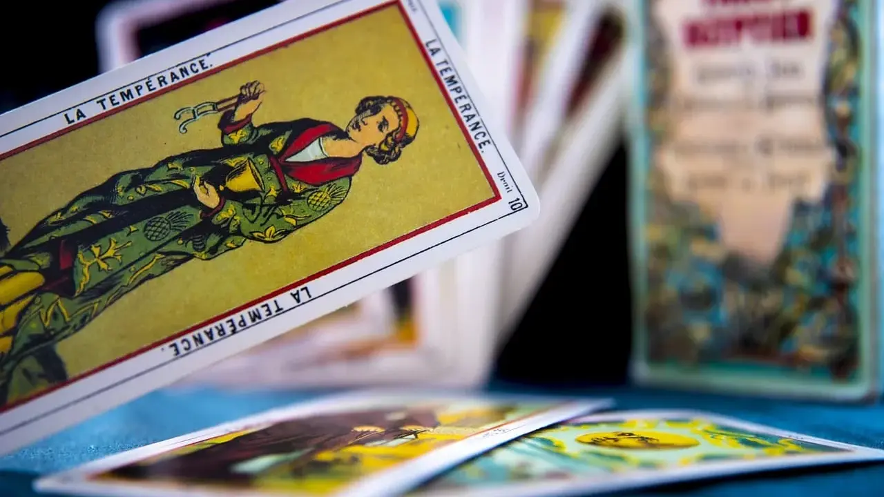 Rozłożone karty tarot 3 karty: "La Tempérance" w centrum, inne karty w tle i pudełko z napisem "Tarot".